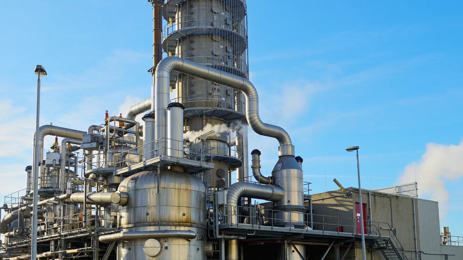A stainless-steel process column and lagged pipework at an industrial plant, under a blue sky