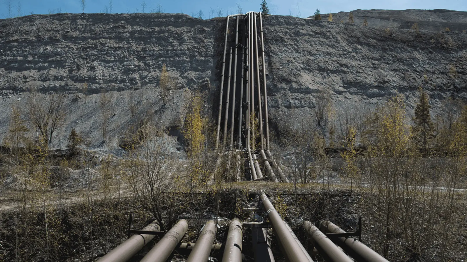 A bank of steel pipelines running up a bare tailings slope at a mine site