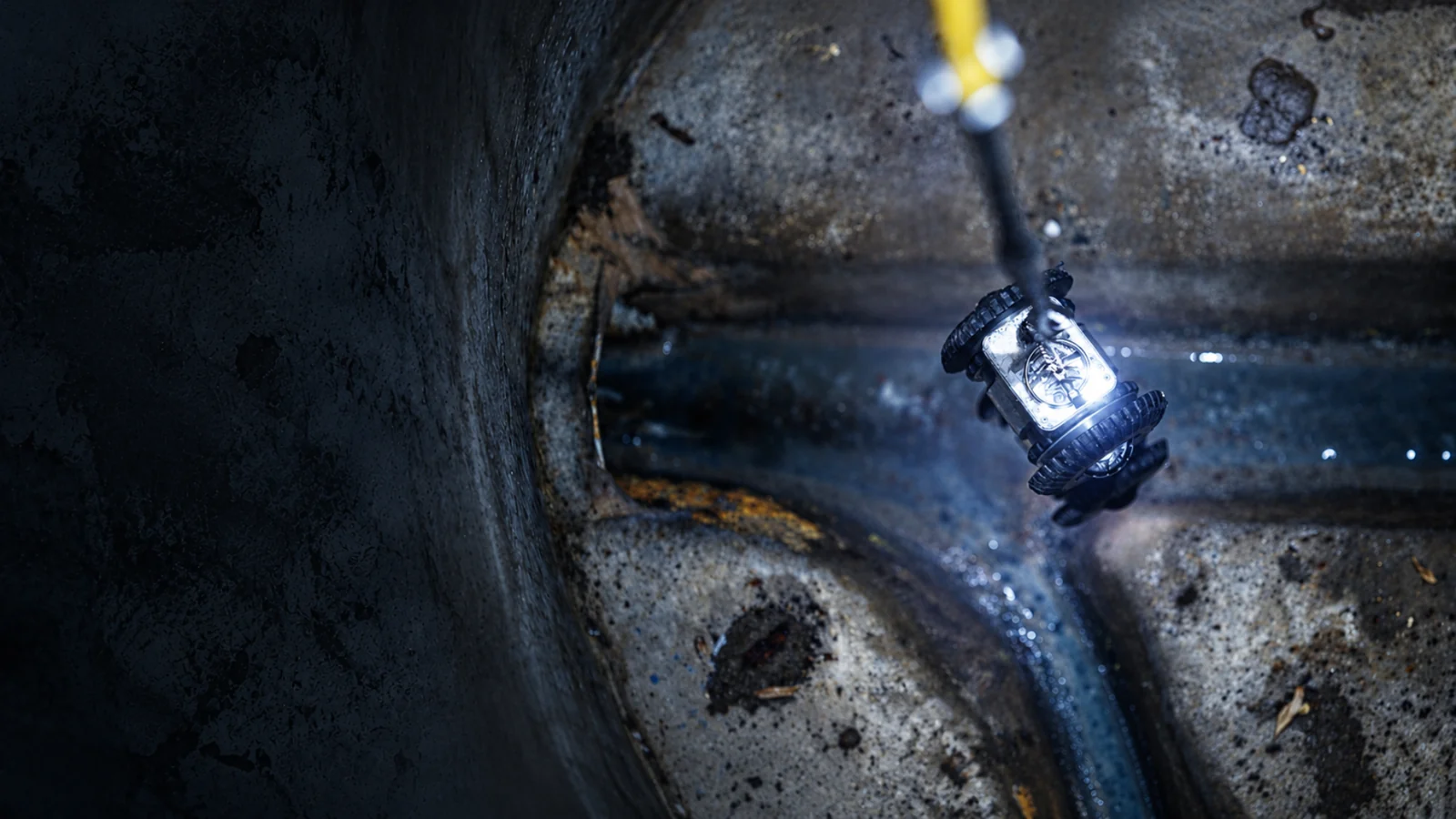 The Ferret hanging from its yellow tether inside a wet concrete chamber, lit by its own lamp