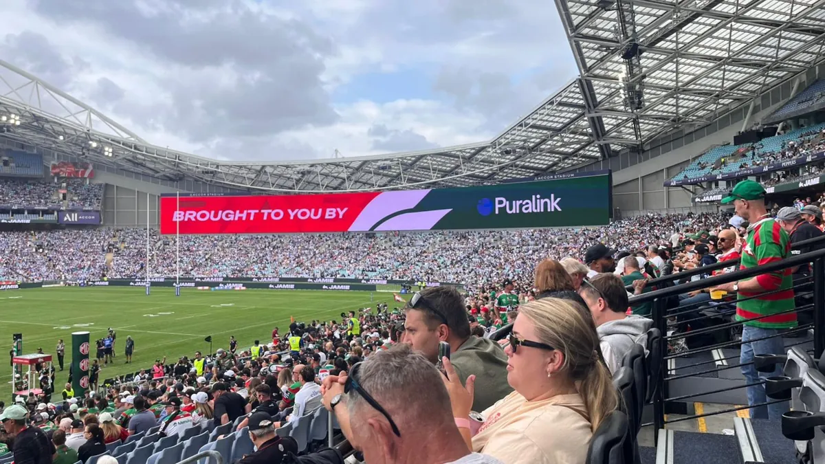 A packed stadium crowd at a Rabbitohs game, with the Puralink logo on the big screen
